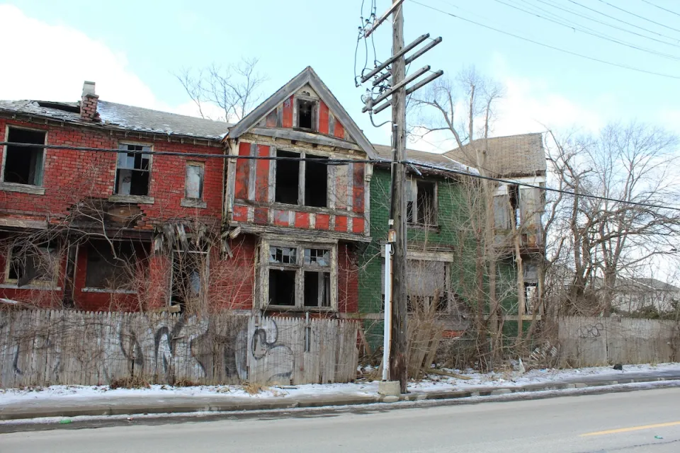 Vacant two-story red brick home in Detroit with missing windows.